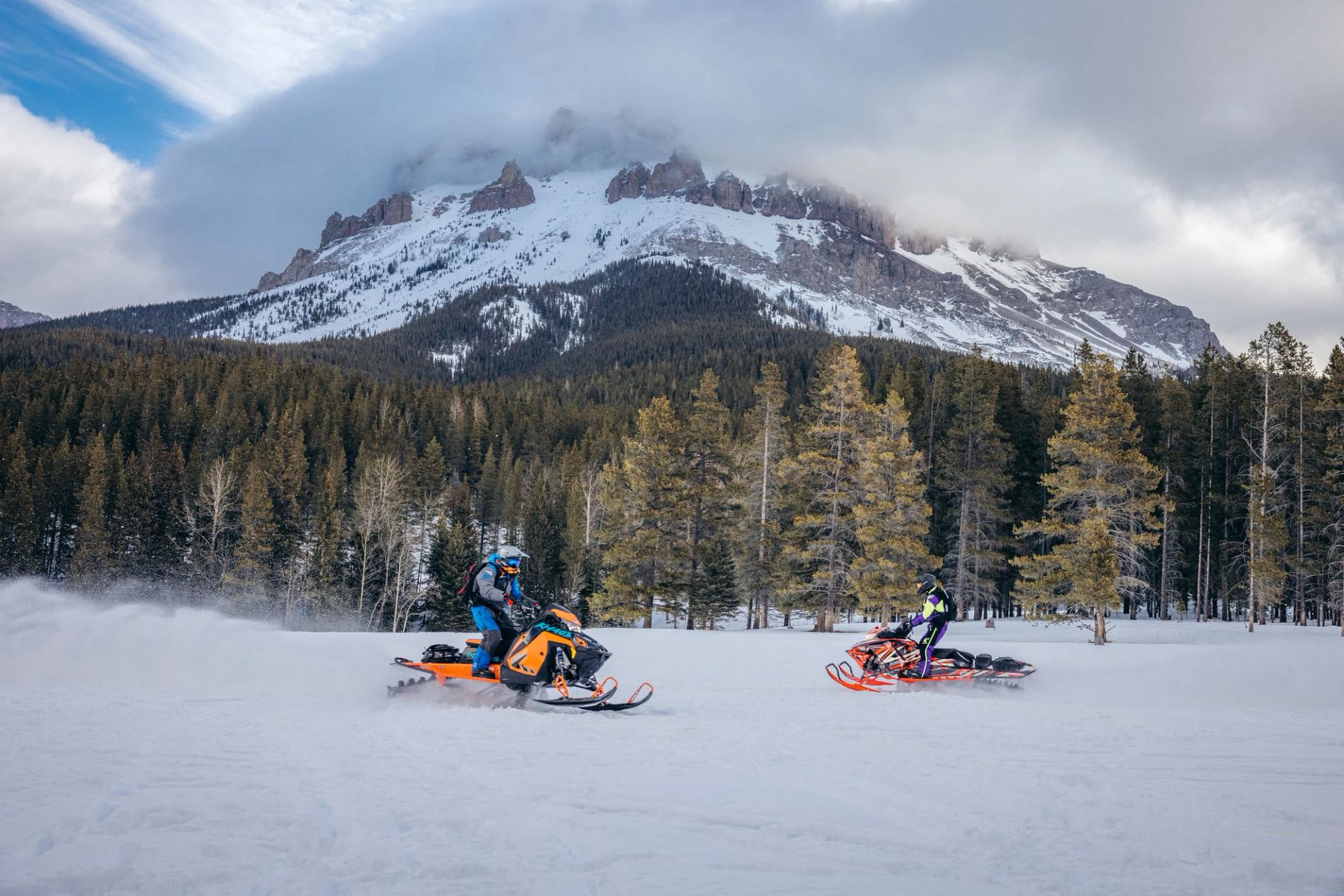 People snowmobiling with mountains in background in the Crowsnest Pass.
