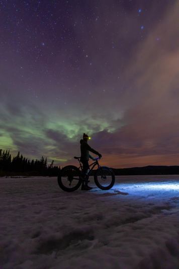 Person fatbiking at night, enjoying the Northern Lights and night sky.