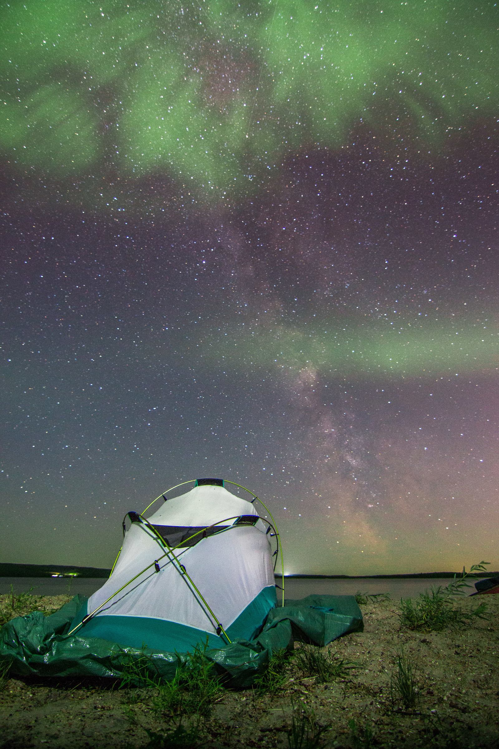 Northern Lights in the nights sky above a camping tent at a lake shore.