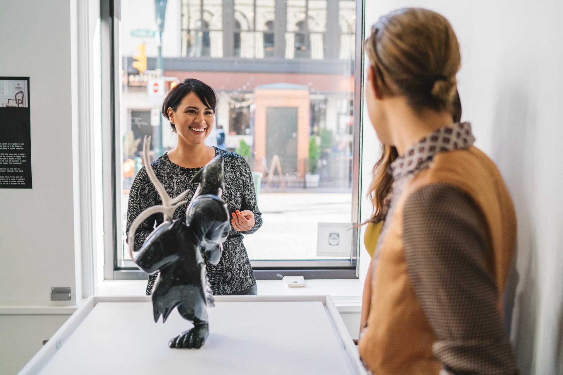 Woman smiling at two workers behind the counter of an art gallery.