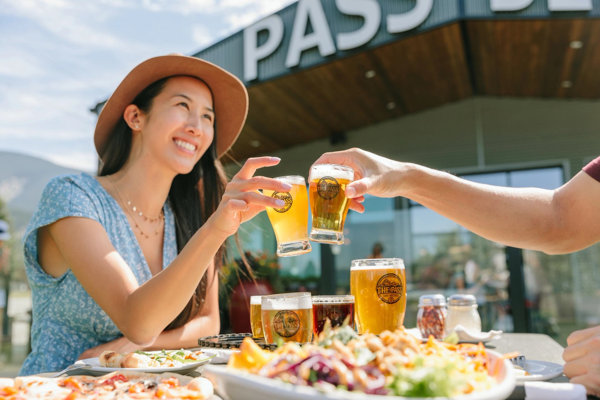 A woman clinking a glass of beer with a friend at The Beer Pass Company in Blairemore Alberta