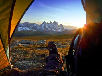 Point of view of a person looking out of a tent onto a mountain view while they are camping in the wildlands while the sun sets