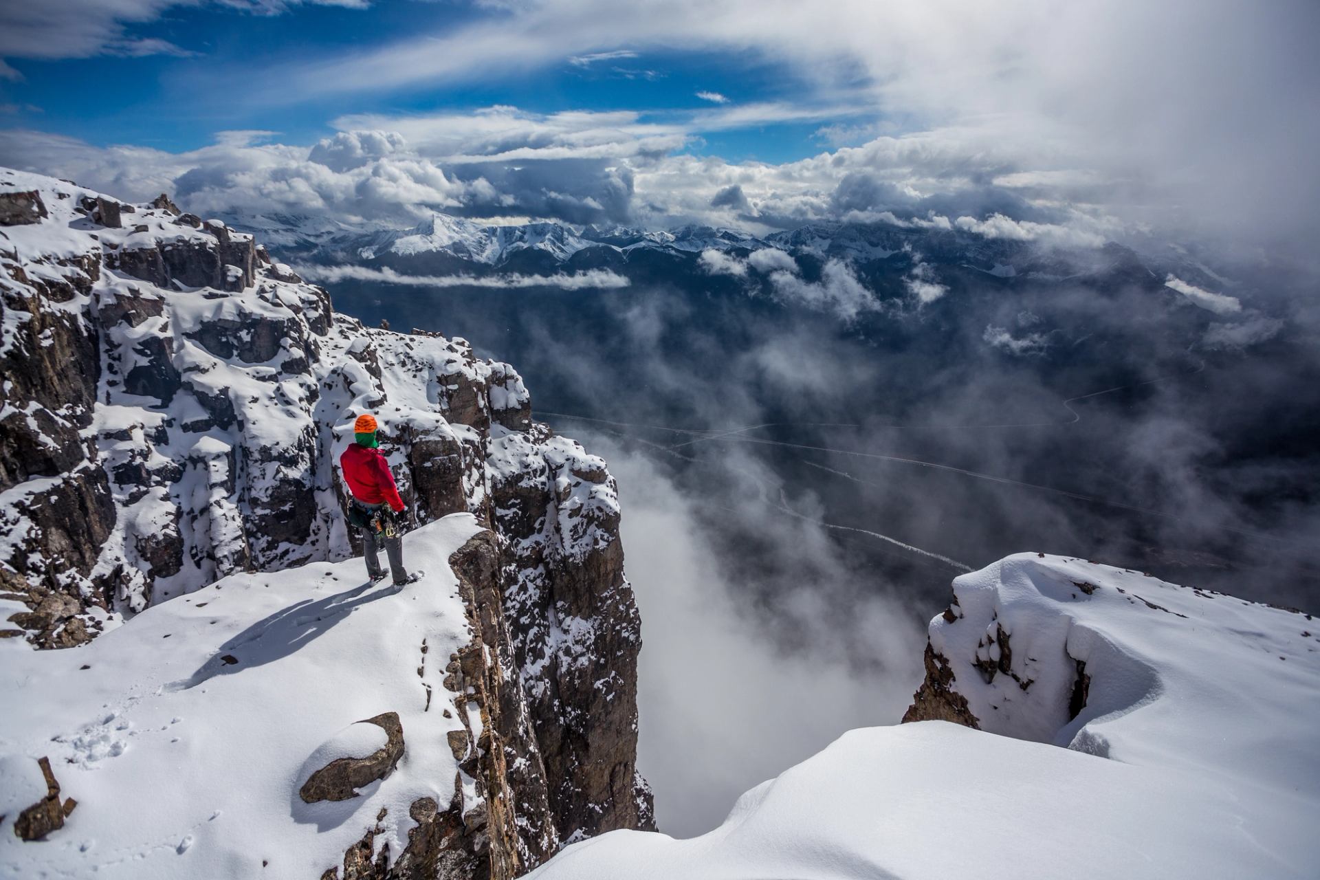 An ice climber standing on a snowy cliff while ice climbing at the top of Eisenhower Tower on Castle Mountain