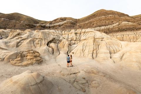 Young couple stand posing fpr a picture beneath the imposing hills of the hoodoo trail Drumheller.