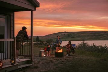 A family enjoys a campfire at sunset at a cabin along the river in Cypress Hills.