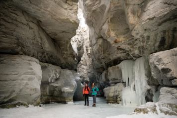 Friend stand in the middle of Maligne canyon taking in the views while ice walking and winter hiking in Jasper National Park