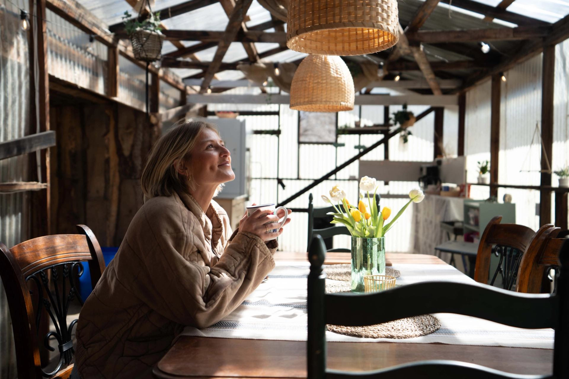 A woman enjoys a coffee in a greenhouse-like patio at Bridgeviews Glamping.