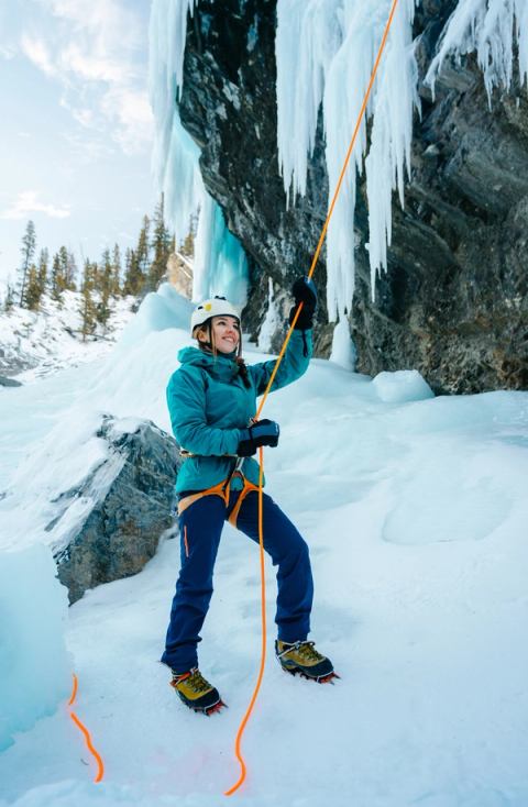 An ice climber stands at the base holding the rope while ice climbing in Nordegg.