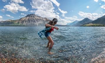 Person with feet in the water skipping rocks into lake in Waterton Lakes National Park.