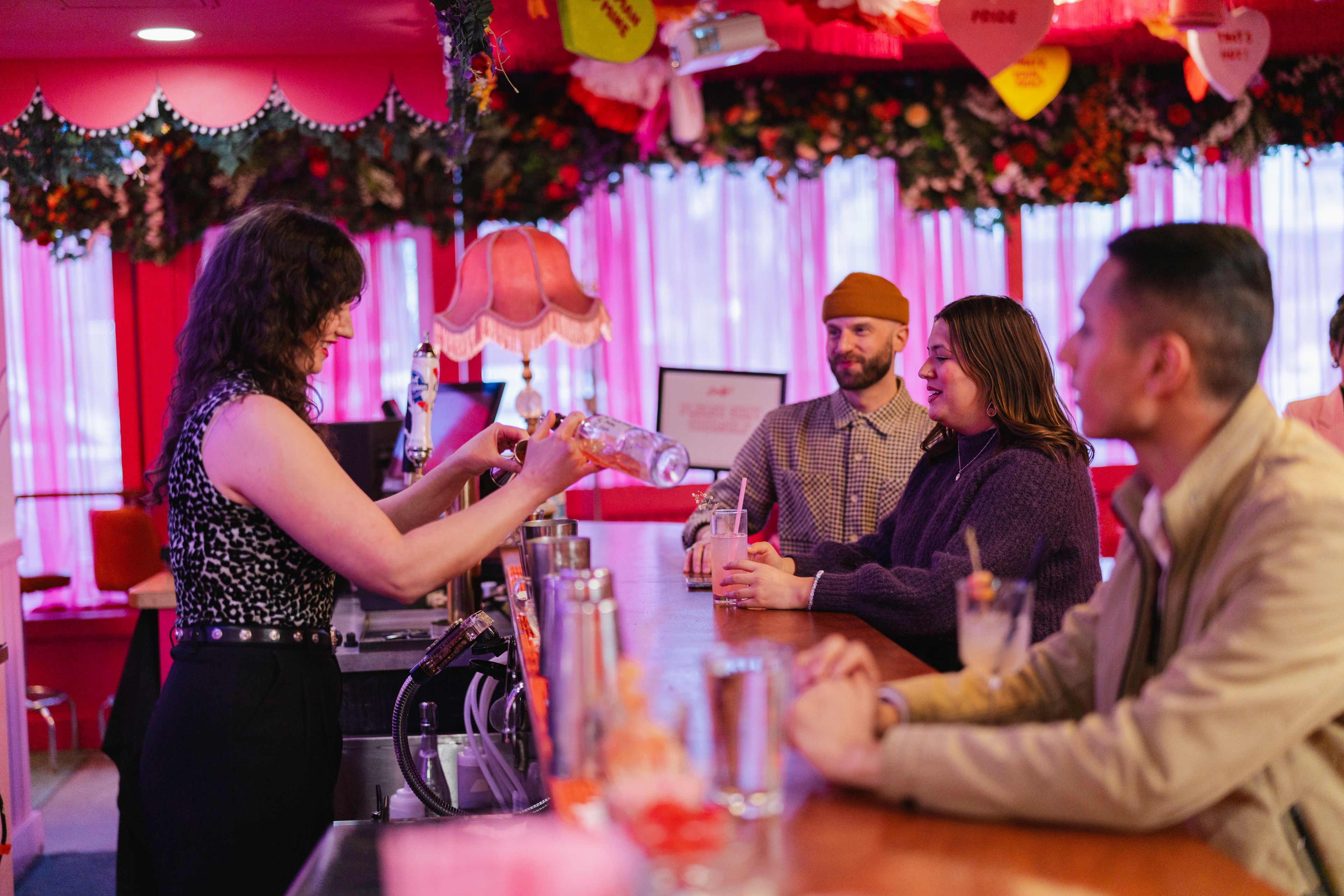 Guests at the bar with drinks while bartender mixes a beverage at Dolly's Cocktail Bar