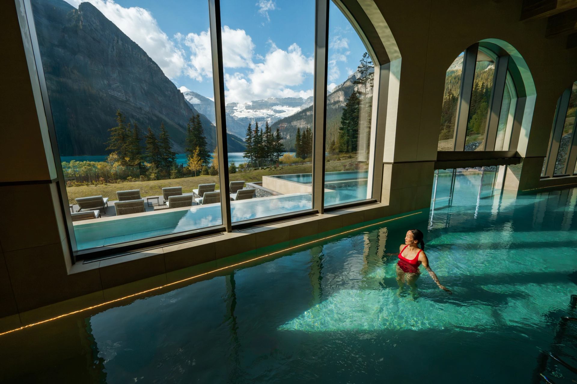 A woman walks through the therapeutic waters at BASIN spa, looking out a large window to Lake Louise and the Rockies.