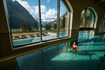 A woman walks through the therapeutic waters at BASIN spa, looking out a large window to Lake Louise and the Rockies.