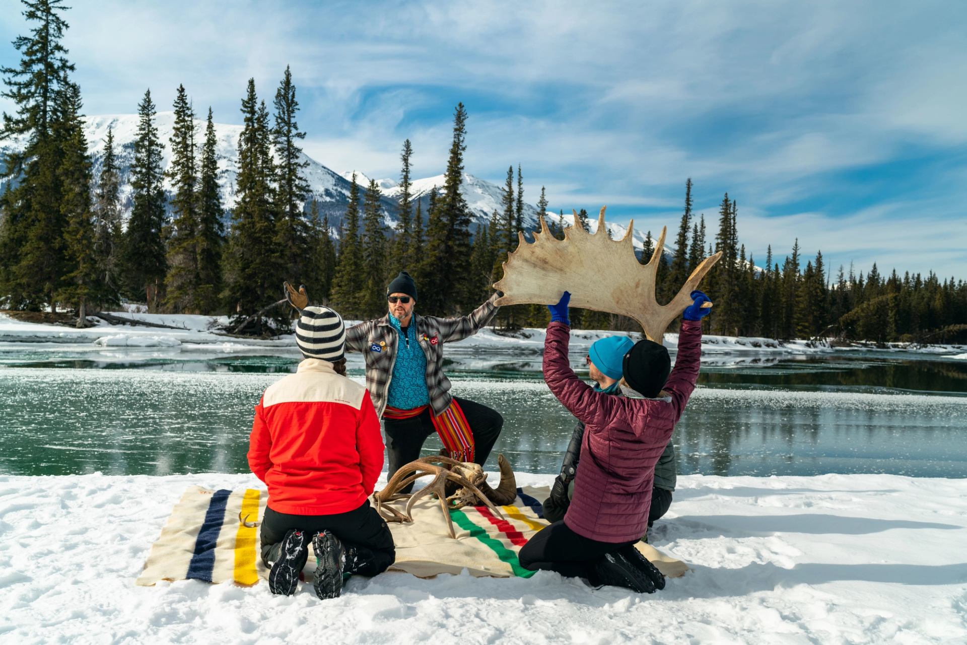 Four people sitting by a river in the winter learning about antlers from a guide.