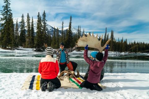 Four people sitting by a river in the winter learning about antlers from a guide.