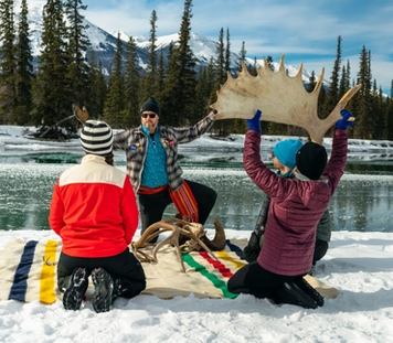 Four people sitting by a river in the winter learning about antlers from a guide.