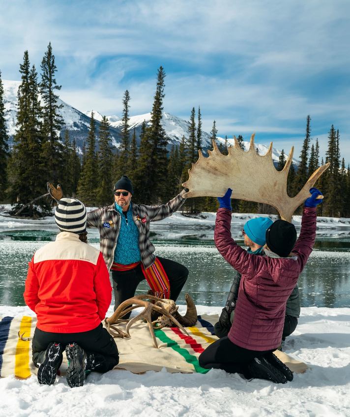 Four people sitting by a river in the winter learning about antlers from a guide.