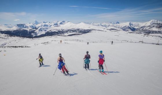 A group of women skiing and snowboarding, jackets tied around their waist, while Spring Skiing at Sunshine Village in Banff National Park.