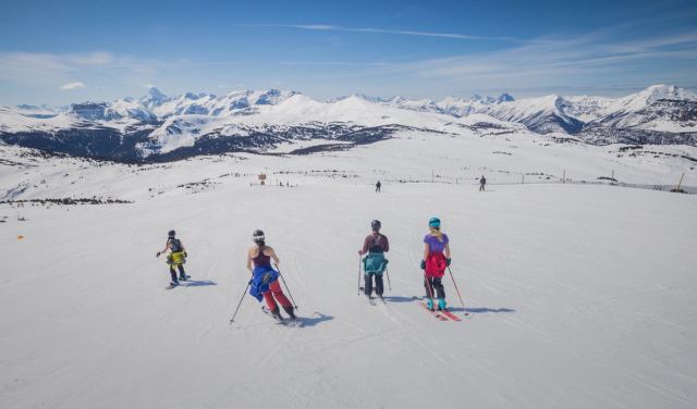 A group of women skiing and snowboarding, jackets tied around their waist, while Spring Skiing at Sunshine Village in Banff National Park.