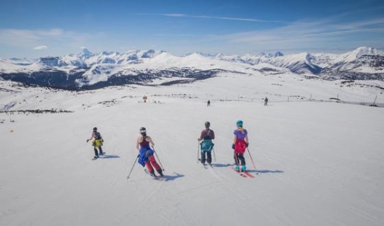 A group of women skiing and snowboarding, jackets tied around their waist, while Spring Skiing at Sunshine Village in Banff National Park.