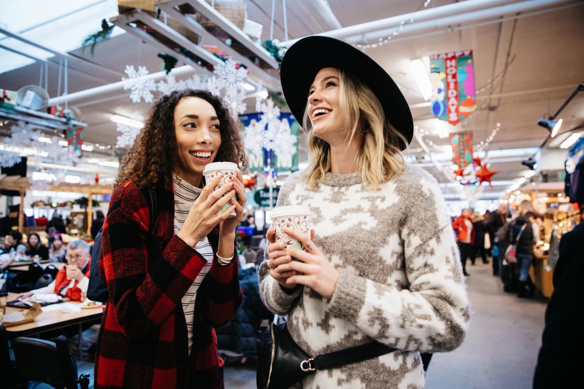 Two women holding coffees shop at at farmers' market.