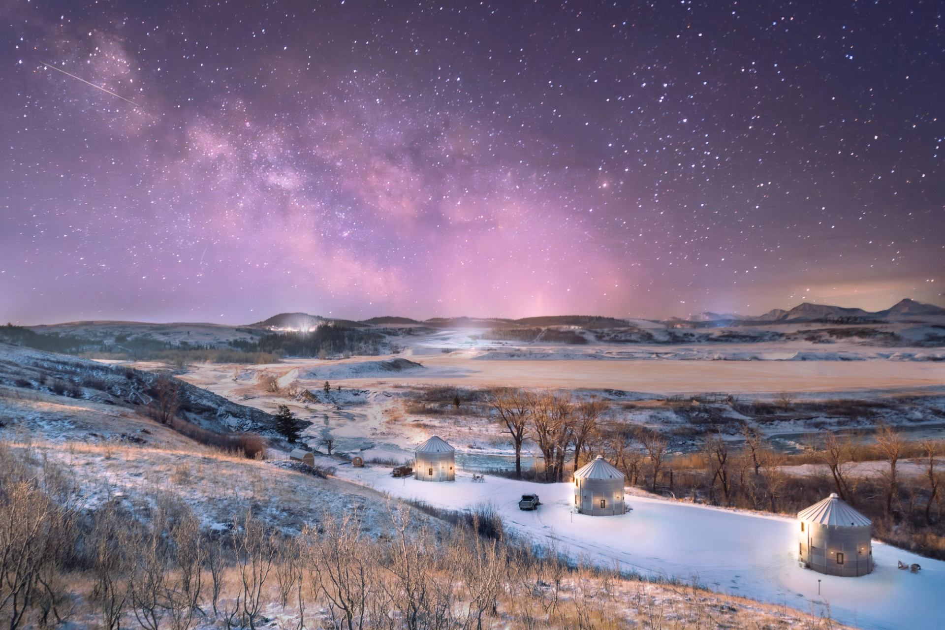 The starry winter sky and milky way glow pink above the Saddle Hill Ranch grain silo cabins.