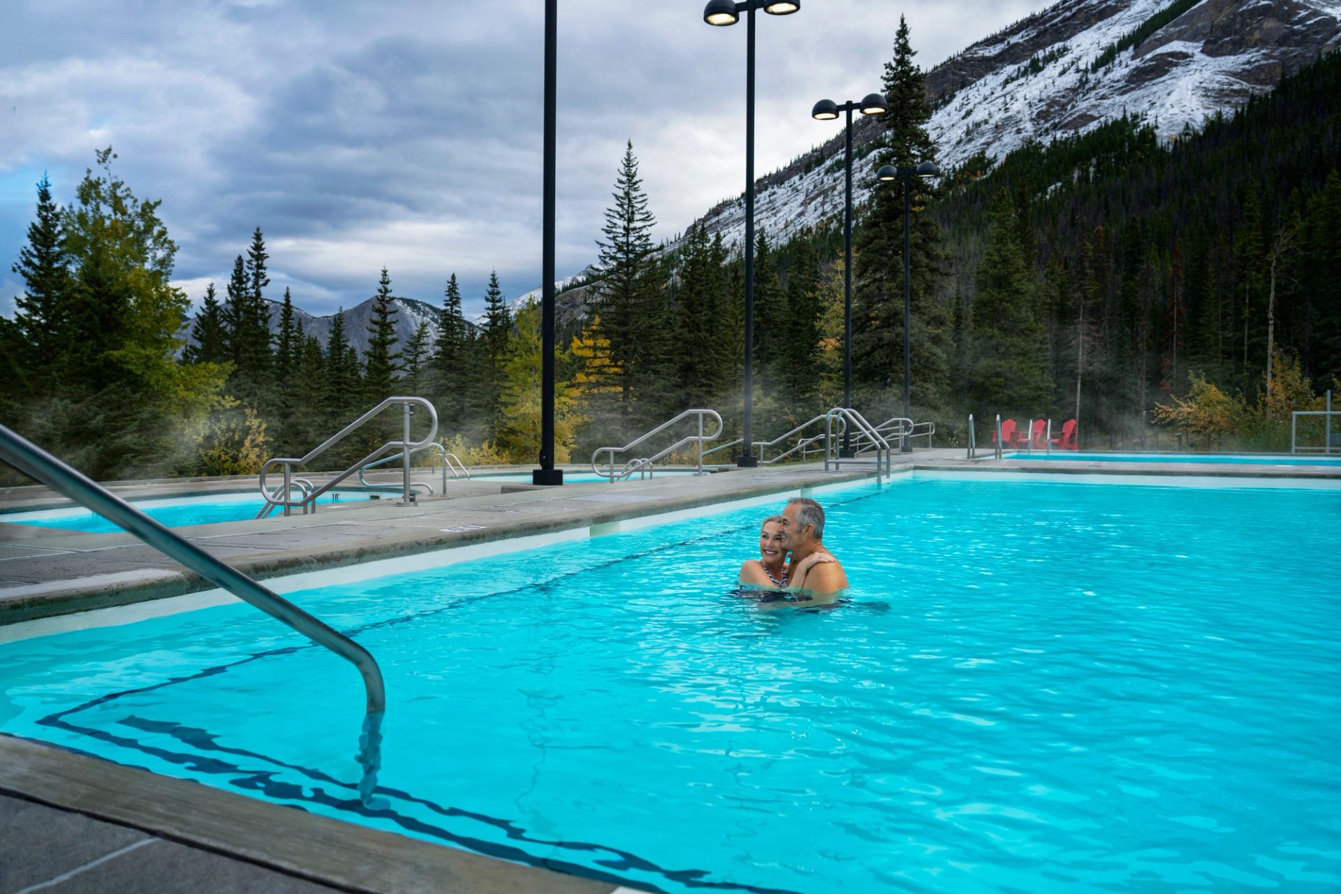 Two people bathe at an empty pool at Miette Hot Springs, surrounded by Rocky Mountains.