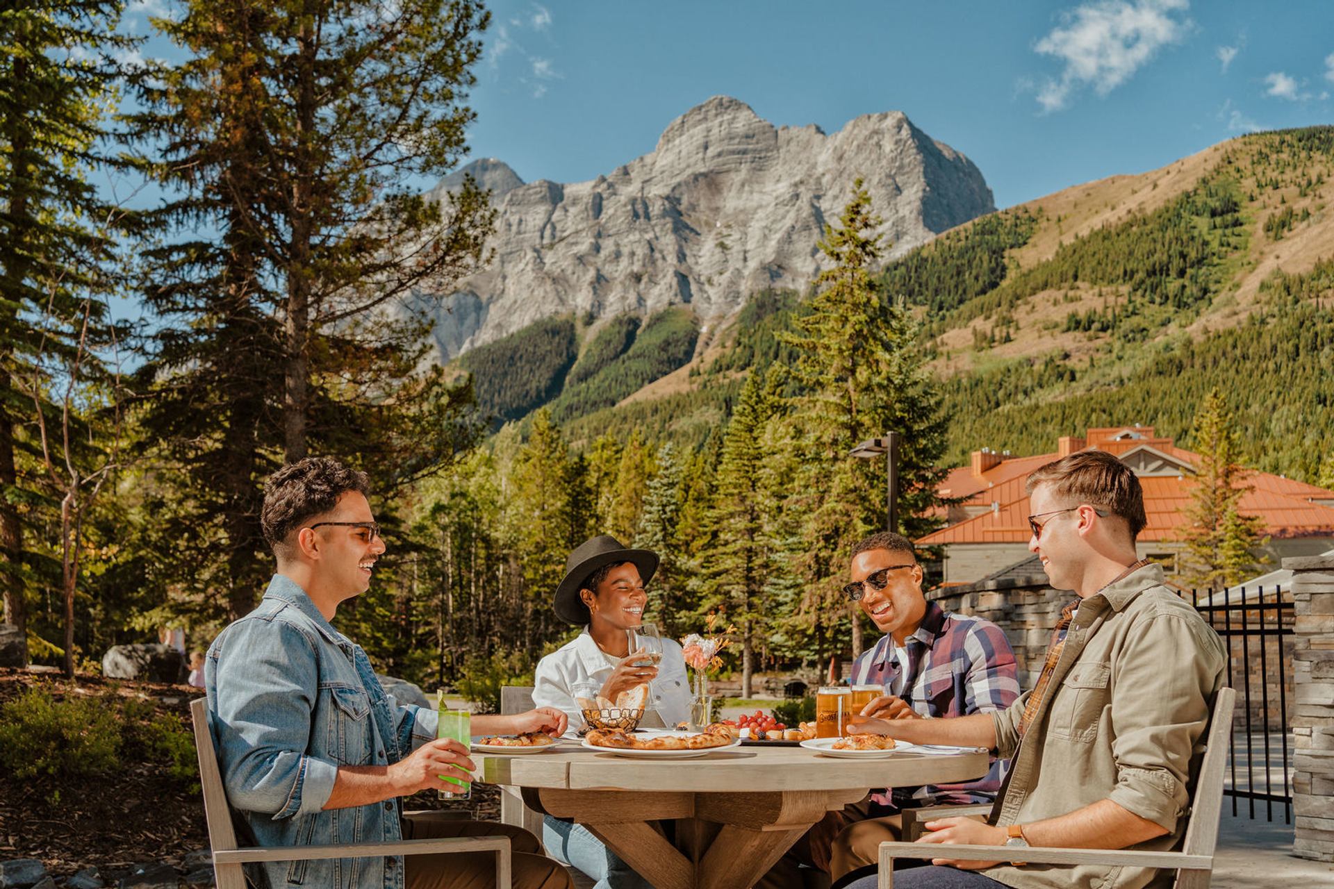 People having a meal at a table outside with a mountain and trees in the background.