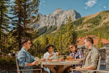 People having a meal at a table outside with a mountain and trees in the background.