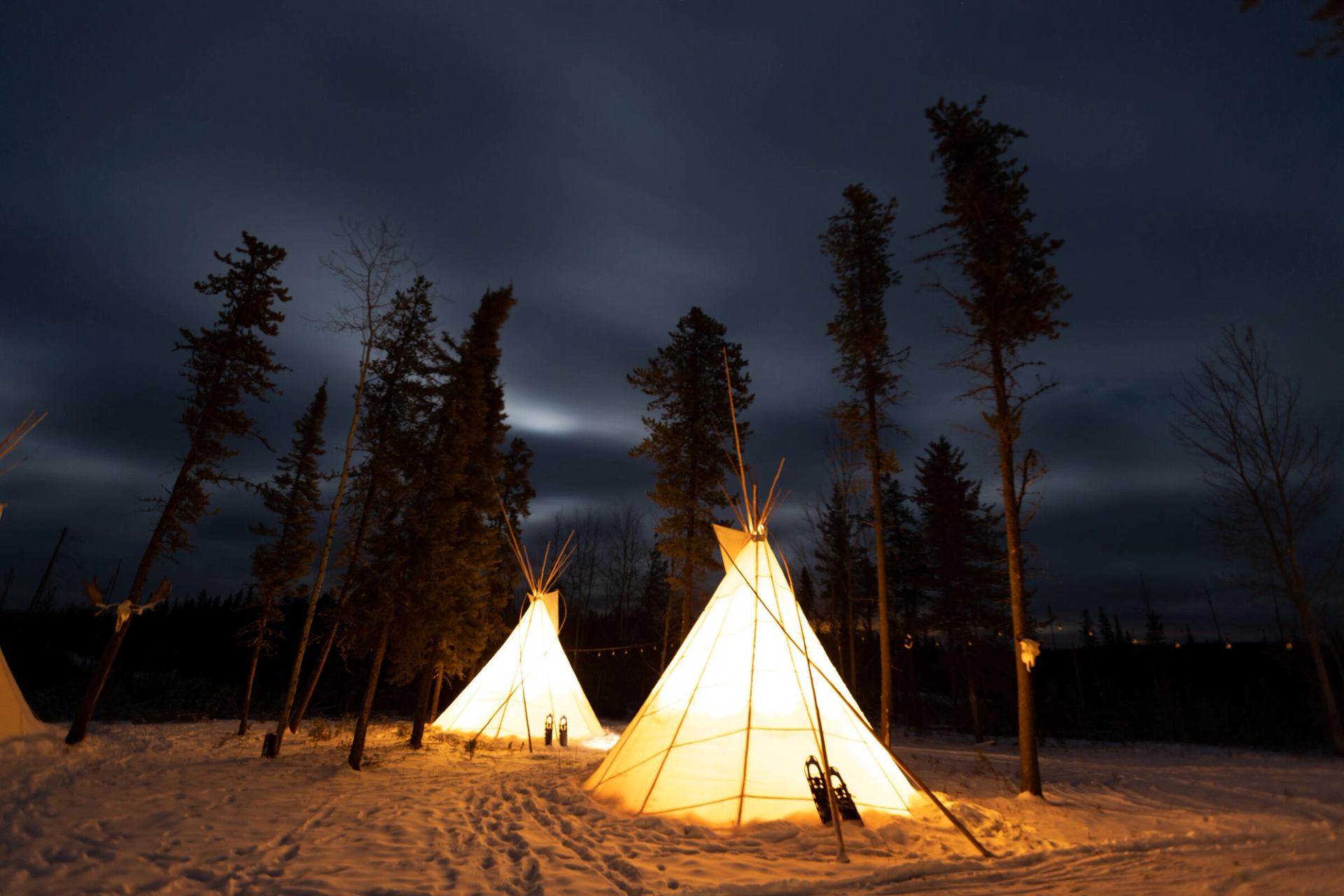 Tipis lit up under the winter night sky at Aurora Borealis Indigenous Village.