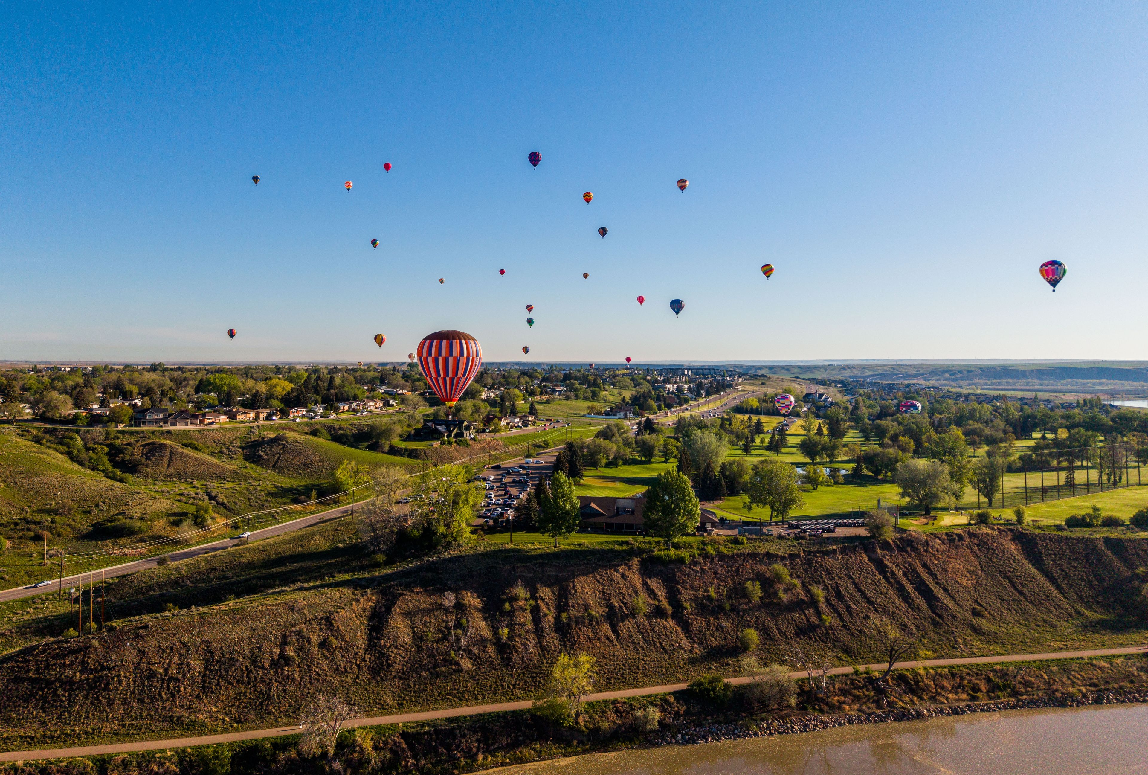 Hot air balloons fly over a river in Medicine Hat.