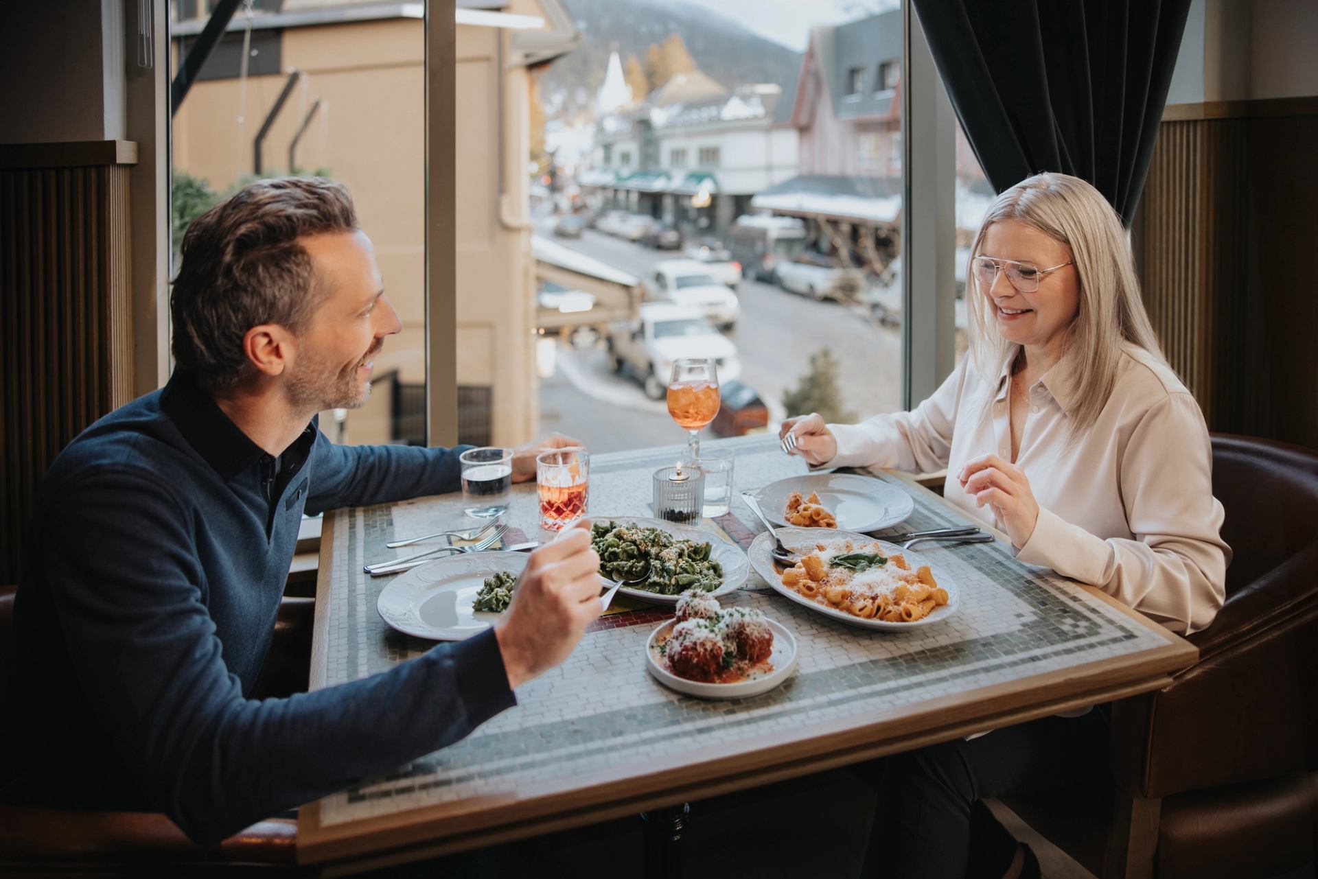 A couple dining at Lupo in Banff with a view of downtown out of the window behind them.