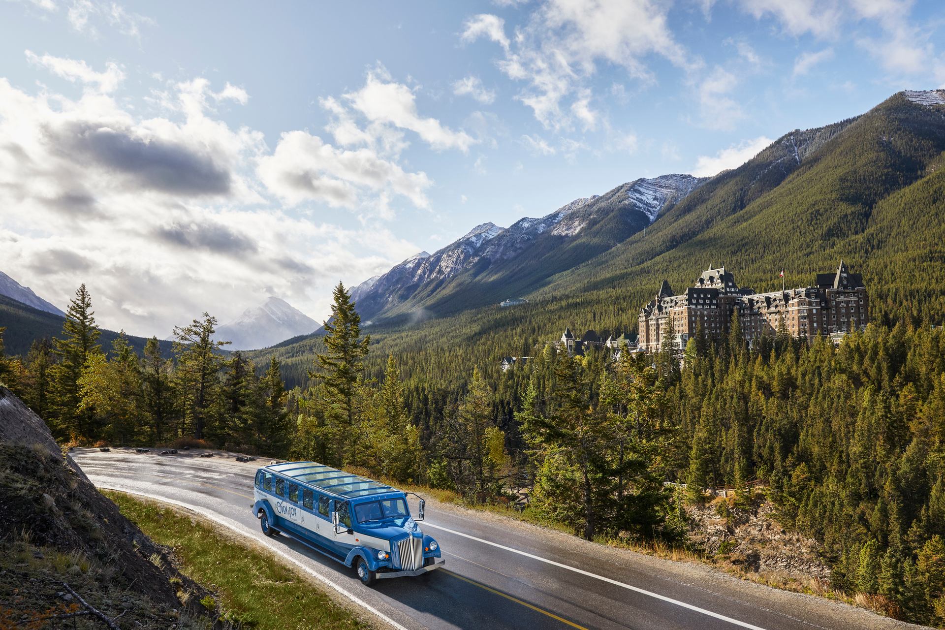 An Open Top Touring vehicle drives by Surprise Corner and the Fairmont Banff Springs in Banff National Park.