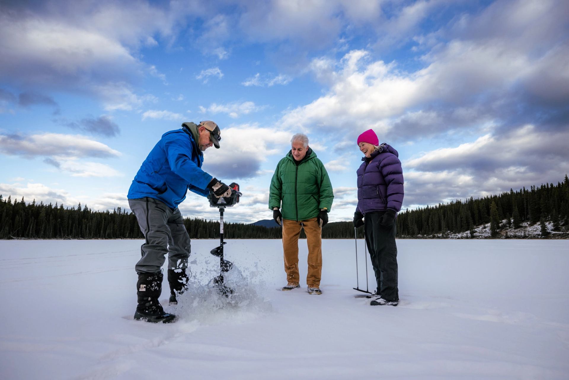 An ice fishing guide with a couple drilling into a frozen lake.
