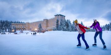 One person pulling another while skating on Lake Louise with Fairmont Château Lake Louise in the background in Banff National Park