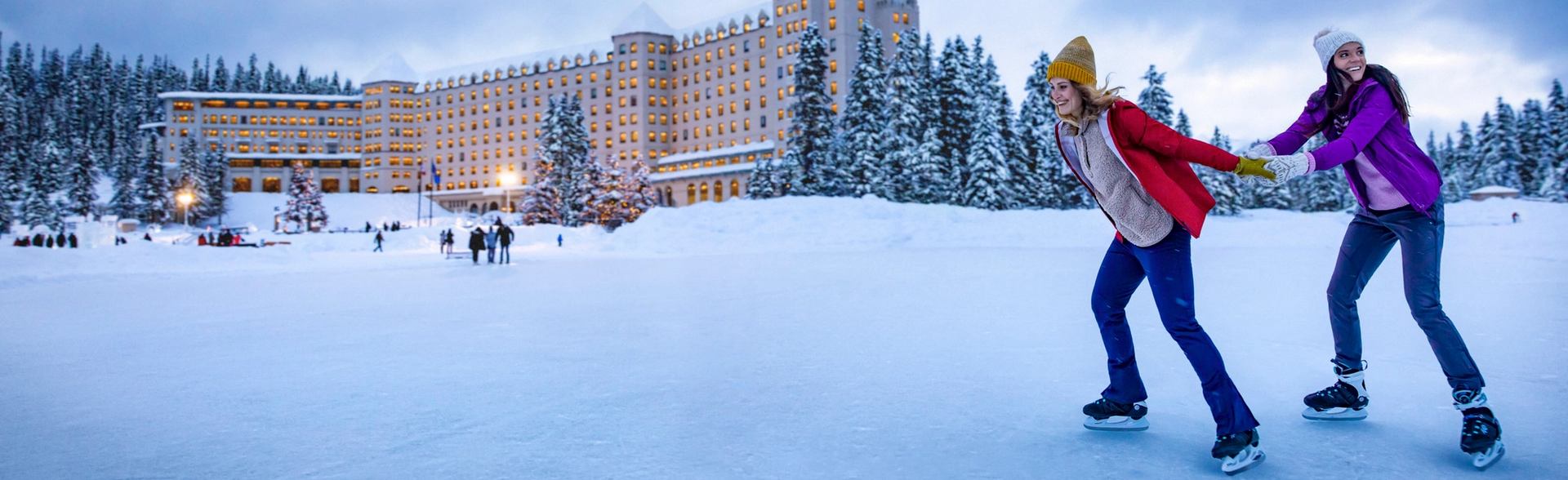 One person pulling another while skating on Lake Louise with Fairmont Chateau Lake Louise in the background in Banff National Park
