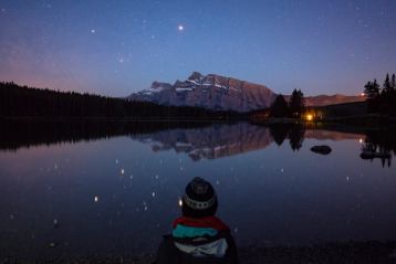 Child looking out at moonlit lake and mountains on a starry night.