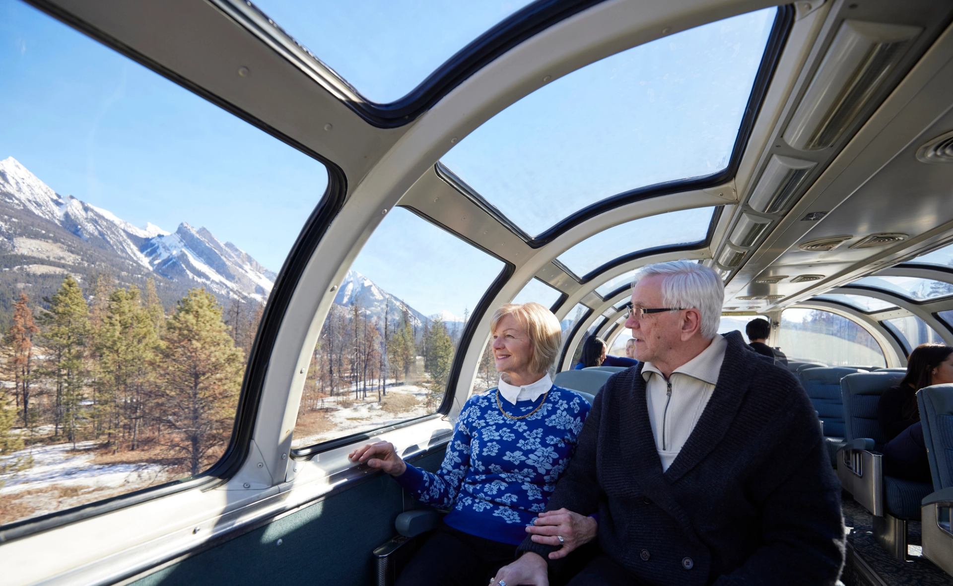 Couple enjoying view of the Rockies from the upper deck dome on a VIA Rail train.