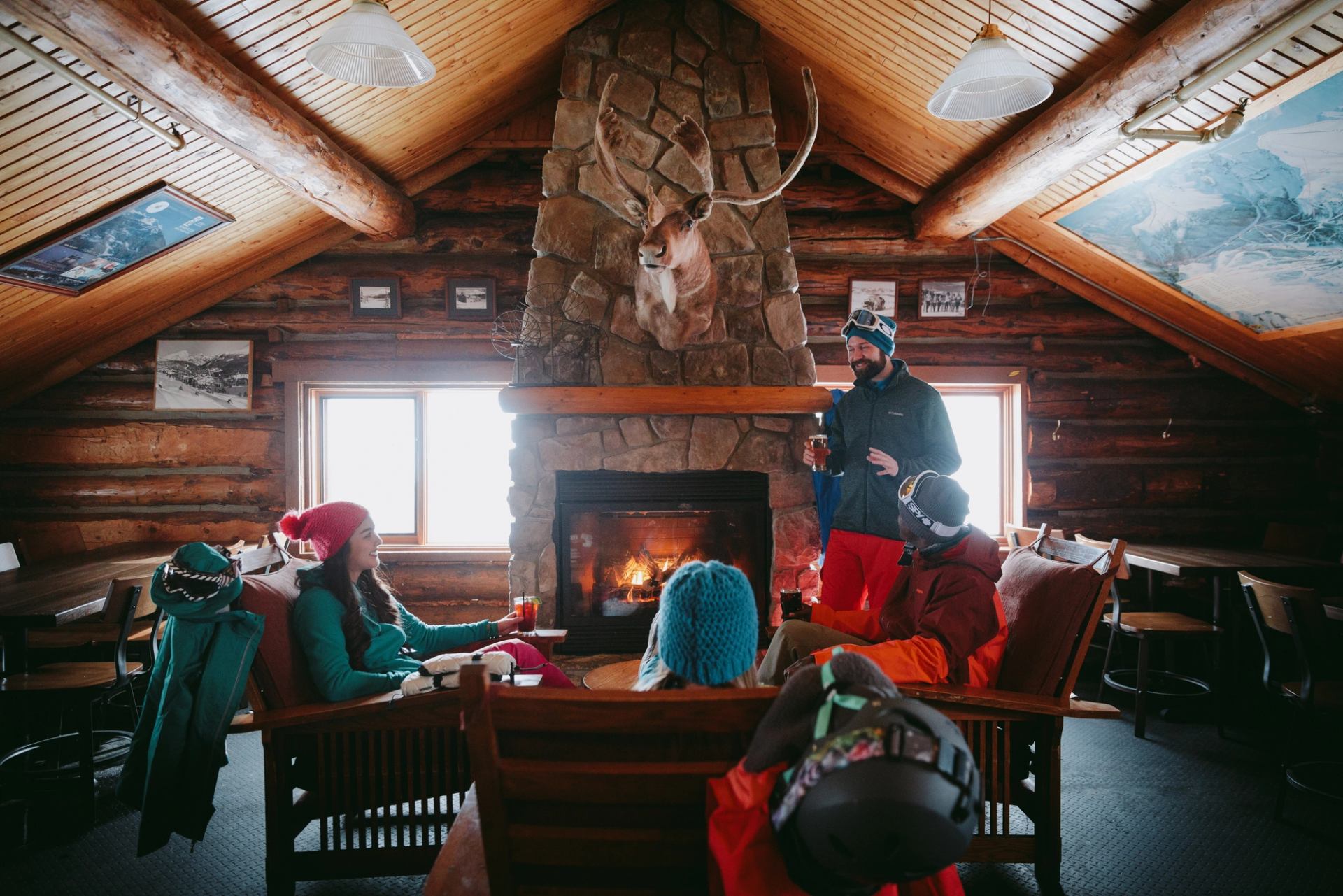 Friends around a fireplace at Mad Trapper's enjoy drinks and snacks after skiing at Sunshine Village in Banff National Park.