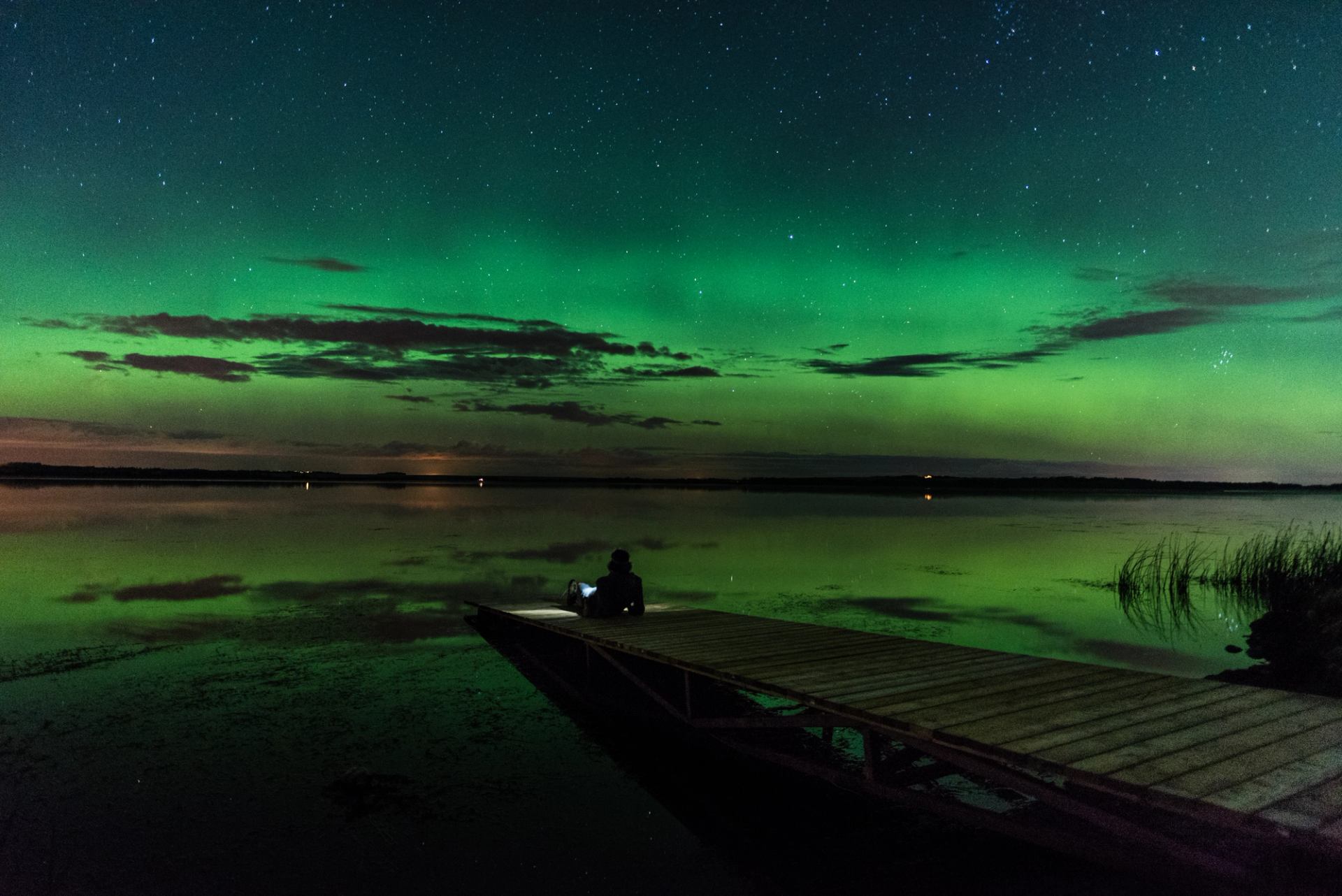 A hiker sits on a pier watching the northern lights.