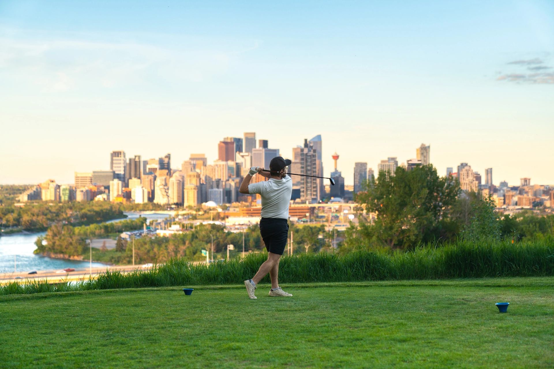 A person golfing at Shaganappi Point Golf Course, with the downtown Calgary skyline in the background.