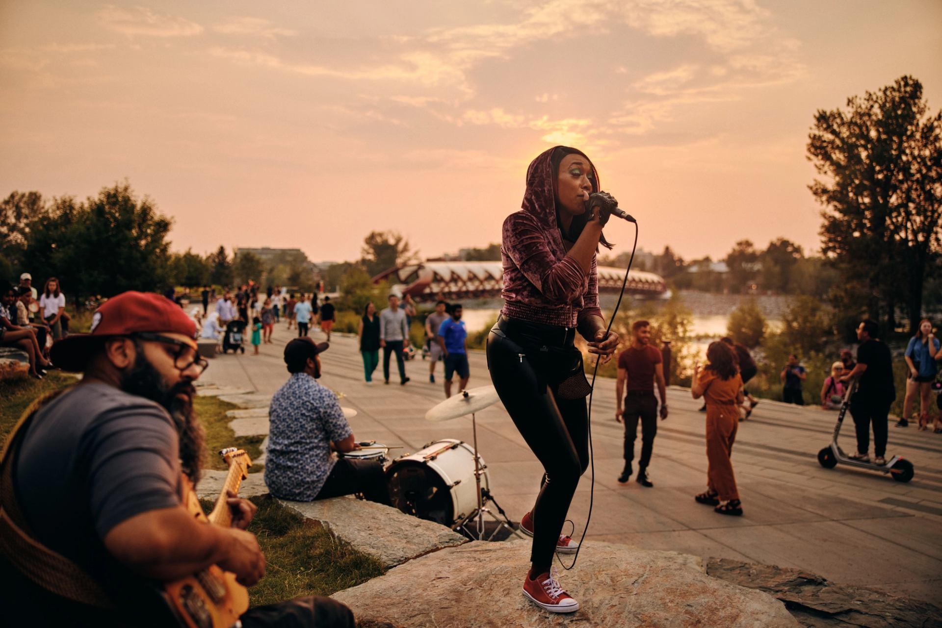 Musicians along a pathway with a bridge and people walking by.