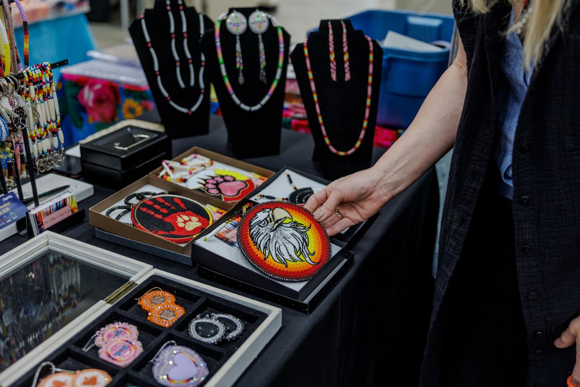A shopper picks up a beaded medallion at an art market during a powwow.