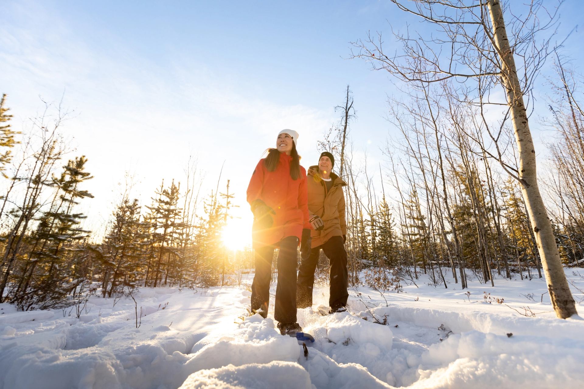 A couple snowshoeing, late day sun shining through the trees at Aurora Borealis Indigenous Village