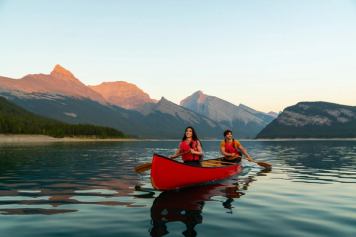 Two people canoe across a lake in the mountains as the final lights hits the Canadian Rockies behind them.
