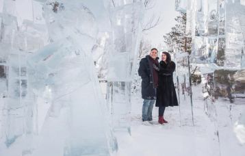 A couple walks through ice sculptures in a park.