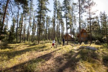 A young couple walking their bikes to a log cabin in the trees at Alpine Village in Jasper National Park