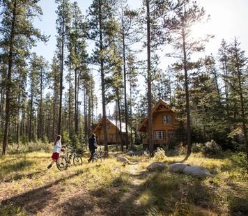 A young couple walking their bikes to a log cabin in the trees at Alpine Village in Jasper National Park