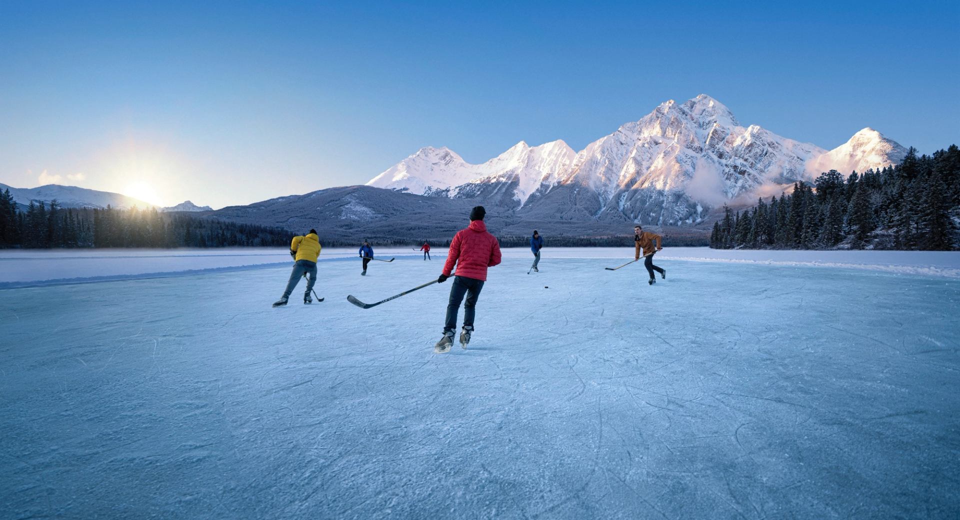 A group of people playing a game of pond hockey as the sun goes down, mountains in the background, on Pyramid Lake in Jasper National Park.