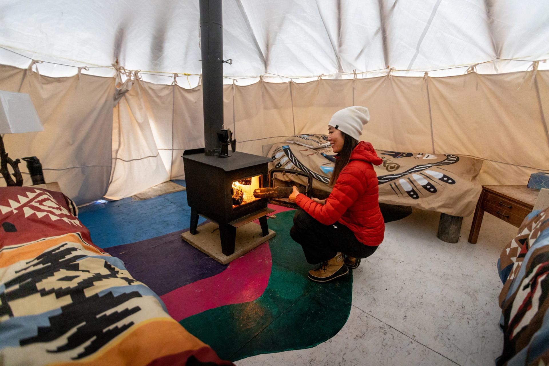 Woman adding wood to fire inside a tipi, at the Aurora Borealis Indigenous Village