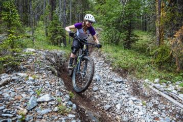 Young girl smiling as she rides down a mountain bike trail through the forest.